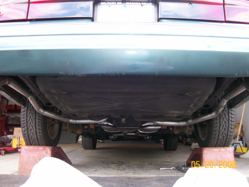 Dual exhaust with two chrome tips under the rear bumper of a green sedan on ramps