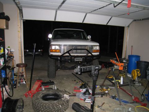 1996 Ford Bronco - A white 1996 Ford Bronco is parked in a garage, equipped with a custom front bumper and winch, surrounded by tools and a spare tire.