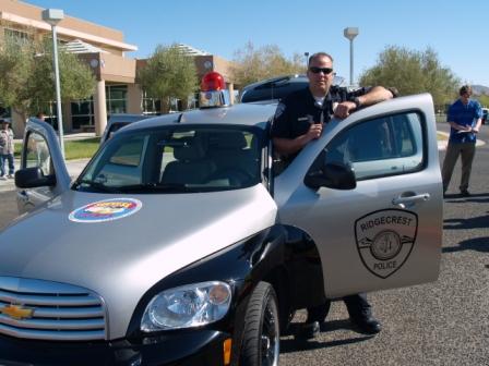 1991 Ford Crown Victoria - A police officer stands by an open car door, with a Ridgecrest Police badge visible on the vehicle.