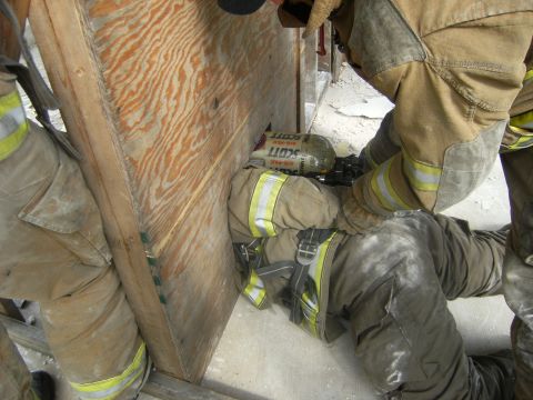 1992 Ford F-150 - Firefighters are seen in a rescue operation, attempting to extract an individual from behind a wooden barrier. The scene depicts a challeng…