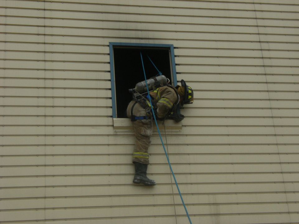 Firefighter in full gear rappelling down the side of a building through a window