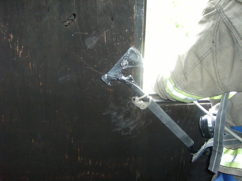 Firefighter using an axe to breach a dark surface near a bright opening