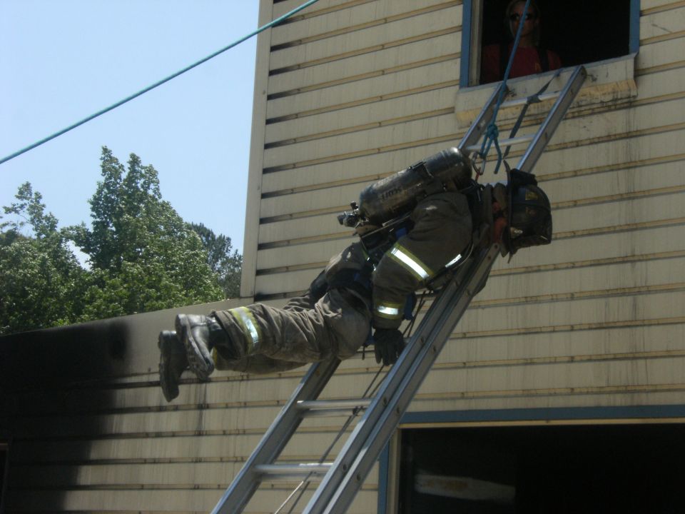 Firefighter in full gear descending a ladder attached to a building
