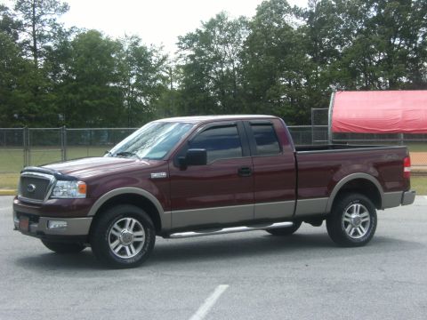 2005 Ford F-150 - Maroon and tan Ford F-150 truck parked on asphalt with trees and a fence in the background.