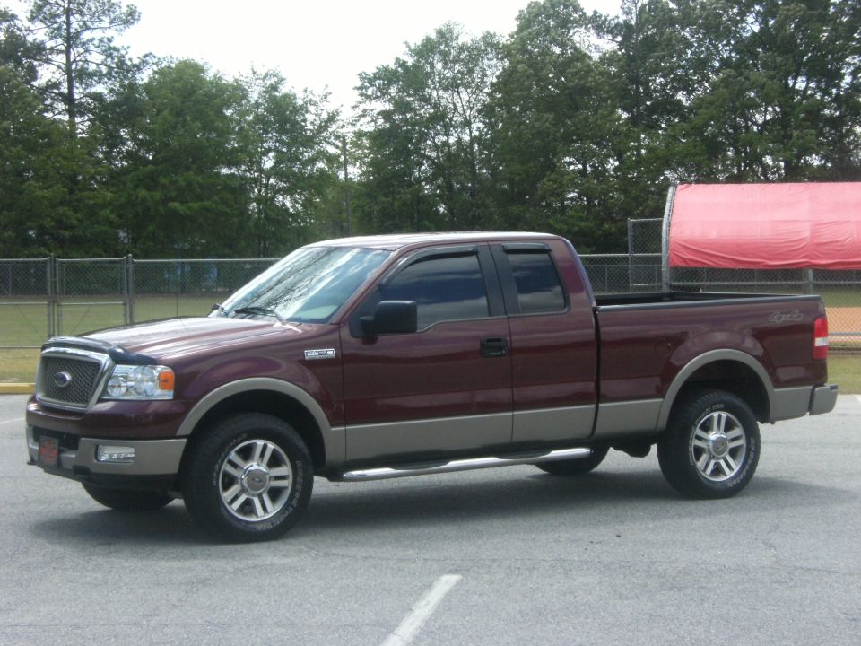 Maroon and tan Ford F-150 truck, driver side view, parked on asphalt