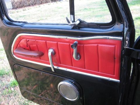 1966 Ford F-100 - The interior door panel of a 1966 Ford F-100 features red upholstered sections and chrome trim around the door handle and window crank.