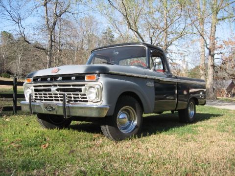 1966 Ford F-100 - Low three-quarter front view of a black mid-1960s Ford F-100 shortbed pickup with gray primer on the hood and fenders, chrome grille with F…