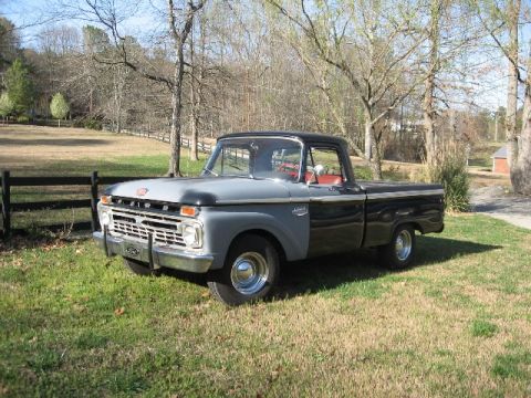1966 Ford F-100 - Driver-side front three-quarter view of a black short-bed Ford pickup with gray primer front fenders and hood, parked on a grassy lawn besi…