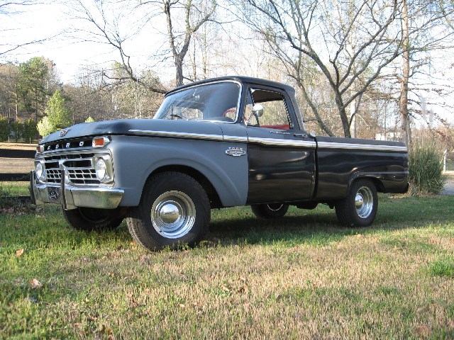 Three-quarter front view of a black 1960s Ford F-100 pickup with gray primer hood