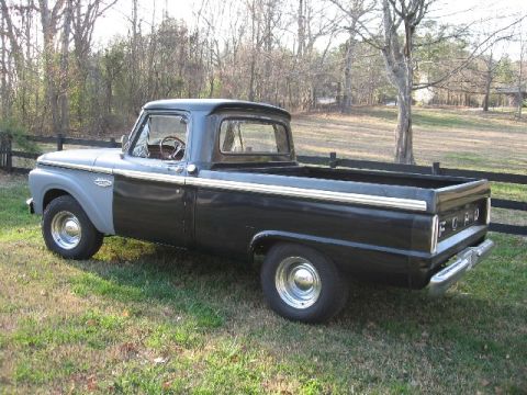 1966 Ford F-100 - Three-quarter rear view of a black mid-1960s Ford F-100 shortbed styleside pickup with gray primer on the cab side and front fender, FORD l…