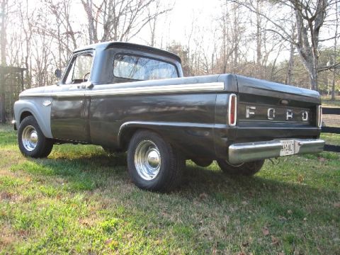 1966 Ford F-100 - Driver-side rear three-quarter view of a black short-bed Ford pickup parked on grass among bare winter trees, showing the styleside bed wit…