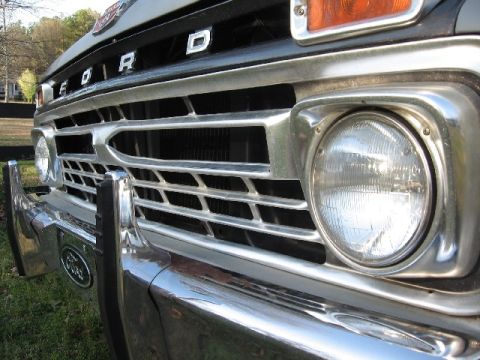 1966 Ford F-100 - Low close-up of the chrome grille on a black mid-1960s Ford pickup, showing the FORD block letters across the hood front, horizontal grille…