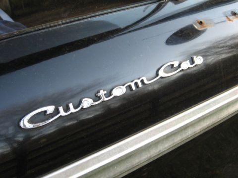1966 Ford F-100 - Tight close-up of the chrome script "Custom Cab" emblem on the black front fender of a vintage Ford pickup, with the stainless body-side tr…