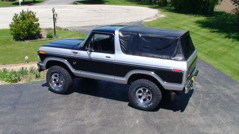 1979 Ford Bronco - This two-tone Ford Bronco features a black soft top and chrome wheels, parked outdoors on a paved surface.