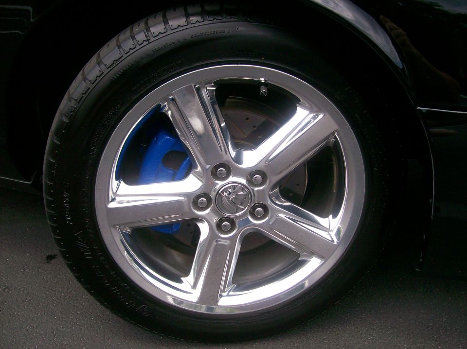 Chrome wheel with blue brake calipers on a black car.