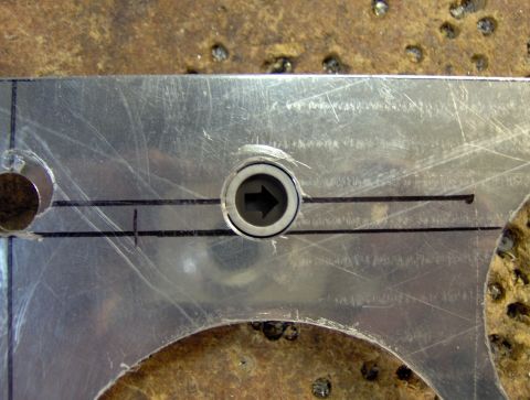 1978 Ford Bronco - A close-up view of a metal bracket with a circular component featuring an arrow pointing left. Two horizontal lines are marked on the brack…