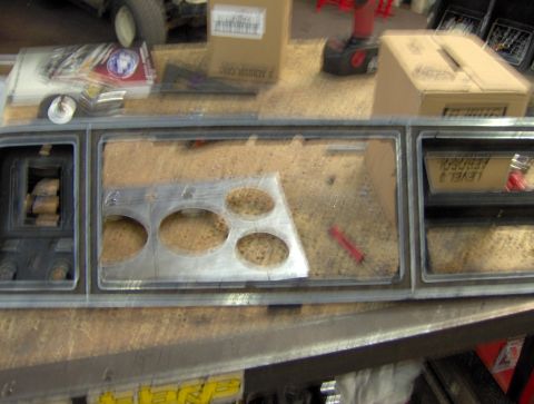 1978 Ford Bronco - A close-up view of a vehicle's dashboard area, showing a cut-out panel with several circular openings. Tools and boxes are visible in the b…