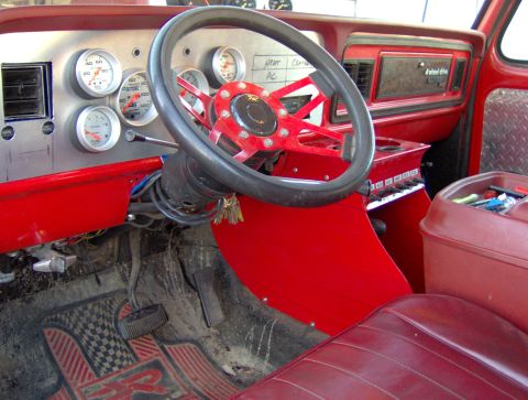 1978 Ford Bronco - The interior of a modified red Ford Bronco features a custom dashboard with multiple gauges, a red steering wheel, and a diamond plate door…