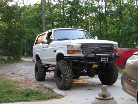 1996 Ford Bronco - Driver-side front three-quarter view of a white full-size Ford Bronco lifted on oversized mud-terrain tires and black steel wheels, parked…