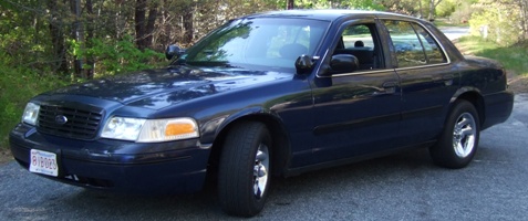 1999 Ford Crown Victoria - Dark blue sedan with chrome wheels parked on a road, showing front and side views.