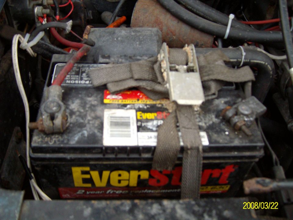 EverStart battery strapped down with a nylon ratchet strap in a dirty engine bay