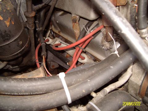 1988 Ford Bronco - Close-up of engine bay wiring showing red wires, braided ground straps and a black heater hose secured by a zip tie.