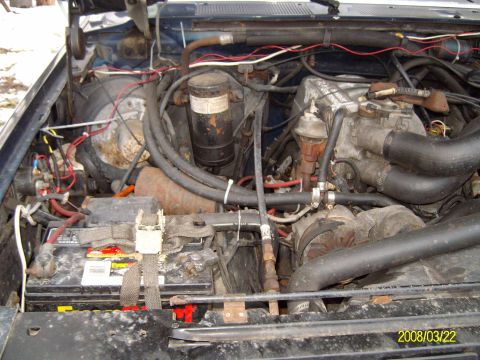 1988 Ford Bronco - Passenger-side engine bay view of a dusty V8 showing the throttle body and upper intake, an alternator, the black canister-style dryer/filt…