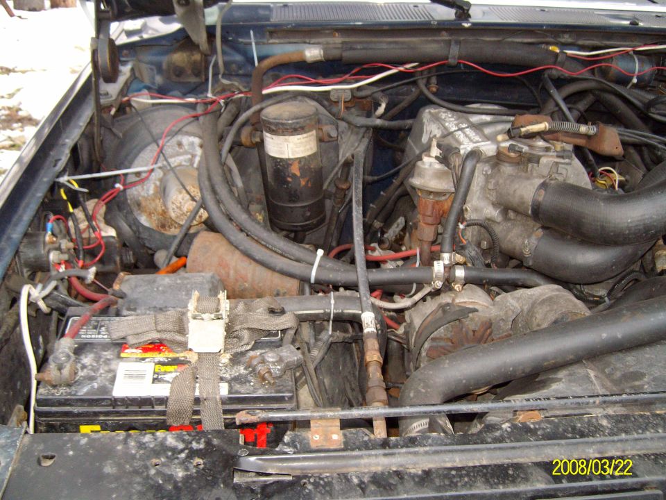 Dusty V8 engine bay from the passenger side with battery, alternator and hoses