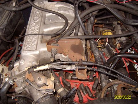 1988 Ford Bronco - Engine bay detail looking down at a cast aluminum Ford EFI upper intake plenum stamped "Electronic Fuel Injection", with a rusty throttle-c…