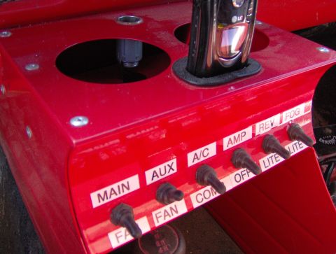 1978 Ford Bronco - A close-up view of a custom-made red dashboard panel various toggle switches and labels for different functions.
