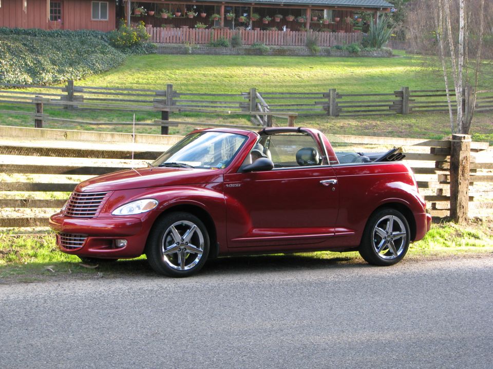 Red convertible Chrysler PT Cruiser parked on a road next to a wooden fence