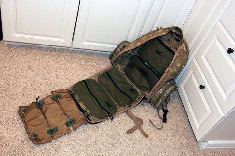 1991 Ford Bronco - An unfolded tactical backpack with camouflage exterior and multiple internal storage compartments is laid out on a carpeted floor next to w…