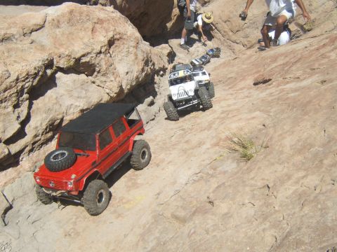 1988 Ford Bronco - Two remote control vehicles navigate a rocky incline, with spectators observing the action.