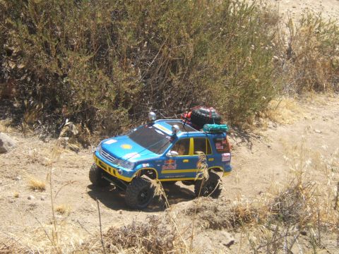 1988 Ford Bronco - RC off-road vehicle with roof rack and spare tire drives on a dusty trail.