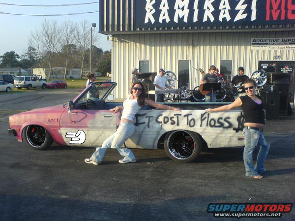 Lowered pink-and-primer convertible spray-painted "It Cost To Floss" with two women posing beside it