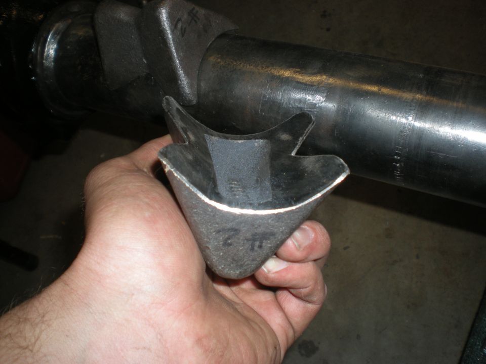 Hand holding a custom metal bracket part with a large metal tube in the background