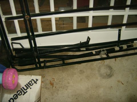2004 Jeep Wrangler - Various black metal bars are piled on a concrete floor, with a pink toy wheel and a cardboard box nearby.