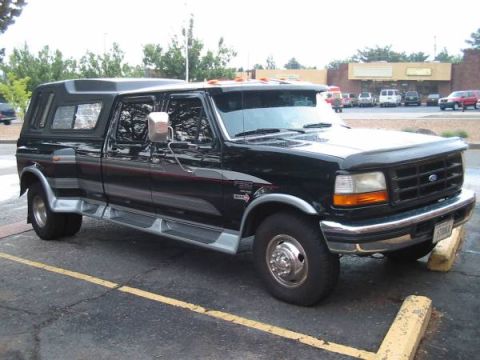 1996 Ford F-250 - This black crew cab pickup truck, likely from the early to mid-1990s, is equipped with a camper shell and dually rear wheels.