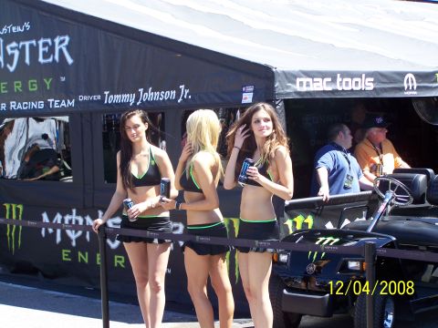 1973 Ford Mustang - A golf cart is visible behind a barrier with Monster Energy branding and three women in bikinis.