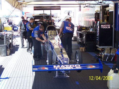 1973 Ford Mustang - A drag racing car is being worked on in a pit stop, with crew members in Matco Tools uniforms surrounding it.