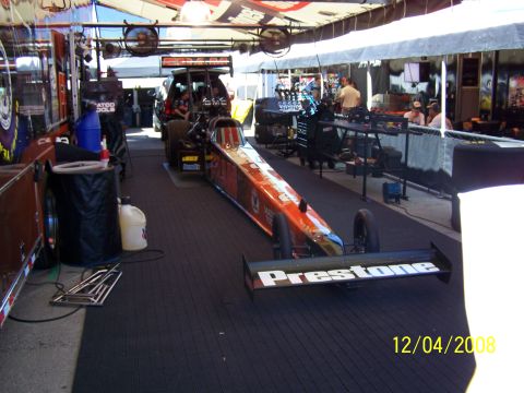 1973 Ford Mustang - A dragster is parked in a pit area, with a support vehicle visible behind it.