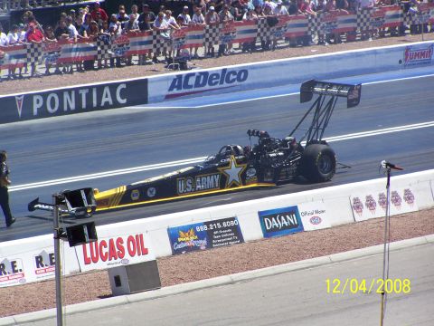 1973 Ford Mustang - A U.S. Army dragster races down the track with spectators watching from the stands.
