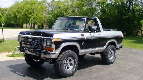 1979 Ford Bronco - This lifted Ford Bronco is parked on a driveway with trees in the background.