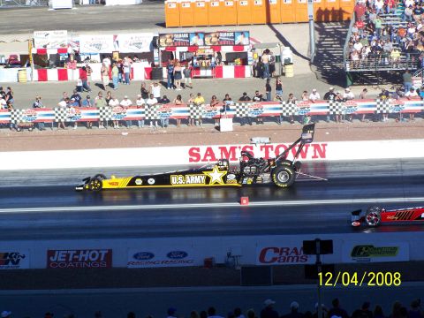1973 Ford Mustang - A dragster with U.S. Army livery competes on a track with spectators in the background.