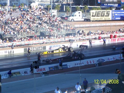 1973 Ford Mustang - Drag racing cars compete on a track with a large crowd in the stands.
