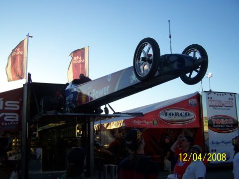 1973 Ford Mustang - A dragster is elevated on a lift, displaying "iPower" branding against a clear sky.