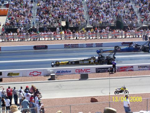 1973 Ford Mustang - Two drag racing cars compete on a track, with a crowd watching from the grandstands.