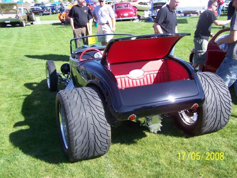 1973 Ford Mustang - A black hot rod with a red interior and large rear tires is displayed on a grassy field at a car show.