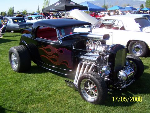 1973 Ford Mustang - A custom black hot rod with flame decals and a powerful exposed engine is displayed at a car show.