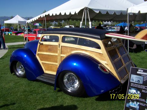 1973 Ford Mustang - A custom woody wagon with a surfboard on its roof is displayed at an outdoor car show.